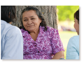 older native american woman talking with others near tree